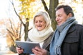 Senior couple with tablet sitting on bench. Autumn park. Royalty Free Stock Photo