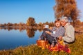 Senior couple taking selfie while having picnic by autumn lake. Happy man and woman enjoying nature and hugging Royalty Free Stock Photo