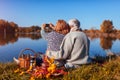 Senior couple taking selfie while having picnic by autumn lake. Happy man and woman enjoying nature and hugging Royalty Free Stock Photo