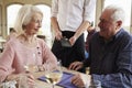 Senior Couple With Waiter Paying Bill In Restaurant