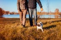 Senior couple walking pug dog in autumn park by river. Happy man and woman enjoying time with pet. Royalty Free Stock Photo