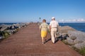 Senior couple walking by the sea. Aged people with a healthy lifestyle. Long lasting couple holding hands. Life expectancy is high