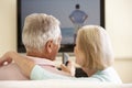 Senior Couple Watching Widescreen TV At Home