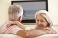 Senior Couple Watching Widescreen TV At Home