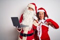 Senior couple wearing Santa Claus costume using laptop over isolated white background with surprise face pointing finger to Royalty Free Stock Photo