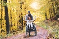 Senior couple with wheelchair in autumn forest.