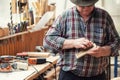 Senior craftsman grinding wooden part with sandpaper grinder machine at carpentry workshop. Mature master polishing details of