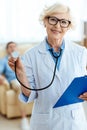 Senior doctor smiling cheerfully and holding stethoscope Royalty Free Stock Photo