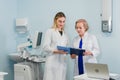 Senior doctor talking with young woman assistant standing in the gynecological office with chair and lamp on the Royalty Free Stock Photo