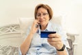 Elderly doubtful woman talking on a mobile phone and holding a bank card in her hand