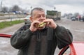 Senior driver gobbling lyulya kebab in lavash near his car