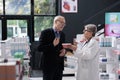 Senior drugstore employee helping elderly customer with cardiology medications explaining medical leaflet