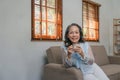 Senior elderly Asian woman sitting on sofa and drinking tea at home. Retirement, health care and ageing concept Royalty Free Stock Photo