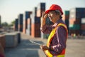 A senior elderly Asian worker engineer wearing safety vest and helmet standing and holding digital tablet at shipping cargo