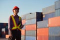 A senior elderly Asian worker engineer wearing safety vest and helmet standing and holding digital tablet at shipping cargo