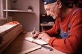 Senior elderly Carpenter writing project notes in woodwork workshop. Profession and small business concept Royalty Free Stock Photo