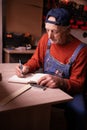 Senior elderly Carpenter writing project notes in woodwork workshop. Profession and small business concept Royalty Free Stock Photo