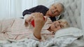 Senior elderly couple wearing pyjamas lying on bed looking on mobile phone laughing and having fun Royalty Free Stock Photo