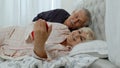 Senior elderly couple wearing pyjamas lying on bed looking on mobile phone laughing and having fun Royalty Free Stock Photo