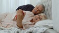 Senior elderly couple wearing pyjamas lying on bed looking on mobile phone laughing and having fun Royalty Free Stock Photo