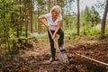 Senior elderly gardener woman digging caring ground level at summer farm countryside outdoors using garden tools rake Royalty Free Stock Photo
