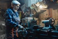 Senior elderly male turner mechanic working on machine tool for metal