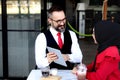 Senior elderly mature business man using tablet and discussing with hijab Muslim women during having a coffee at outdoor cafe, Royalty Free Stock Photo