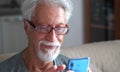 A Senior elderly 70s man using smart phone calling online looking at screen relaxing at home Royalty Free Stock Photo