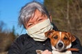 Senior elderly woman with gray hair wearing face mouth nose cotton cloth home made virus mask posing with her Jack Russell dog