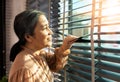 Senior Elderly woman look at window in evening. Grandmother wait patiently for home coming person with sad lonely depress. Asian