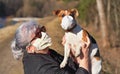 Senior elderly woman with virus face mask holding her Jack Russell terrier dog an hands, she wear simple cloth respirator as well Royalty Free Stock Photo