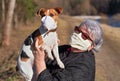 Senior elderly woman with virus face mask holding her Jack Russell terrier dog an hands, she wear simple cloth respirator as well Royalty Free Stock Photo