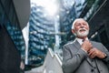 Senior entrepreneur adjusting necktie while standing outside office on sunny day Royalty Free Stock Photo