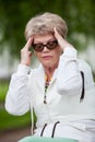 Senior European woman with tension headache sitting on a bench after jogging in park