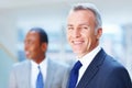 Senior executive smiling with colleague in background. Focus on older Business man with colleague in background. Royalty Free Stock Photo