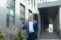 Senior experienced gray-haired businessman outside office, smiling and happy using phone Royalty Free Stock Photo