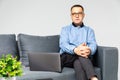 Senior experienced psychologist is sitting on sofa in his office and smiling