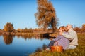 Senior family couple having picnic by autumn lake. Happy man and woman enjoying nature and hugging Royalty Free Stock Photo