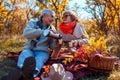 Senior family couple having tea pouring it from thermos in fall forest. Happy man and woman enjoying picnic outdoors Royalty Free Stock Photo