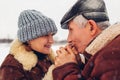 Senior family couple walks in park in snowy winter weather. Elderly man warms wife& x27;s hands with breath