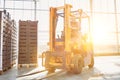 Senior farmer driving forklift in greenhouse with yellow lens flare in background