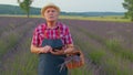 Senior farmer grandfather growing lavender, holding digital tablet and examining harvest in field