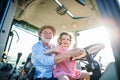 Senior farmer with small granddaughter sitting in tractor, driving.