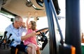 Senior farmer with small granddaughter sitting in tractor, driving.