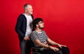 Senior father with young son in wheelchair in a studio on red background. Royalty Free Stock Photo