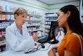 Senior female chemist advising dosage intake of medication given to young woman patient over the counter standing in Royalty Free Stock Photo