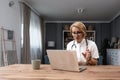 Senior female doctor working from home office from home practice sitting in white doctor\'s coat with stethoscope Royalty Free Stock Photo