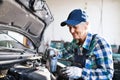 Senior female mechanic repairing a car in a garage. Royalty Free Stock Photo