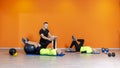 Senior fit couple doing weight lifting workout exercise laying at the gym isolated on orange background with personal trainer. Royalty Free Stock Photo