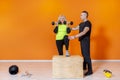 Senior fit woman doing weight lifting workout exercise standing at the gym isolated on orange background with pesonal trainer. Royalty Free Stock Photo